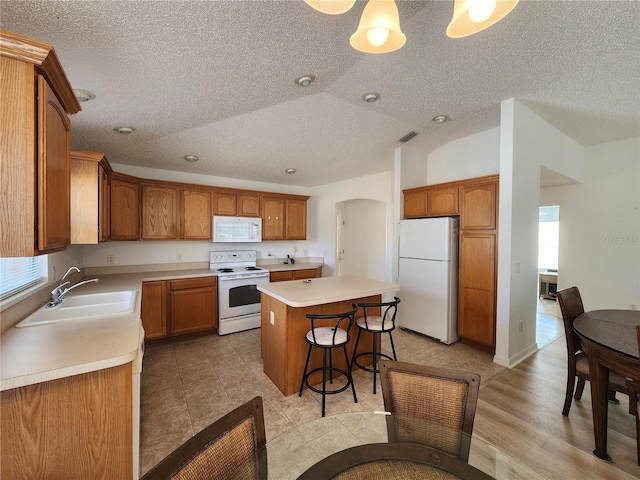 kitchen with a kitchen bar, sink, vaulted ceiling, a kitchen island, and white appliances