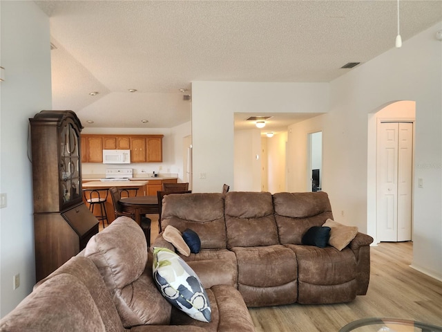 living room with light hardwood / wood-style flooring, a textured ceiling, and vaulted ceiling