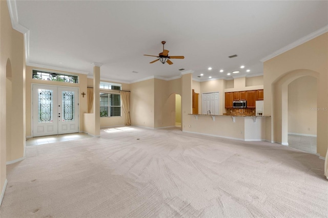 unfurnished living room featuring french doors, light carpet, crown molding, and ceiling fan