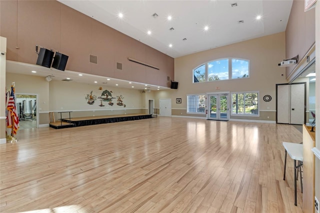 exercise area with light hardwood / wood-style floors, french doors, and a high ceiling