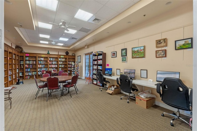 carpeted home office featuring ceiling fan, a drop ceiling, and a raised ceiling