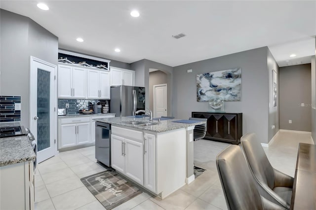 kitchen with sink, appliances with stainless steel finishes, white cabinetry, light stone counters, and a center island with sink