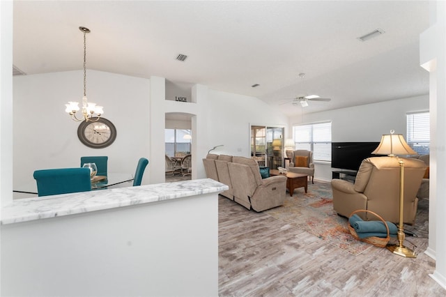 living room with lofted ceiling, ceiling fan with notable chandelier, and light wood-type flooring