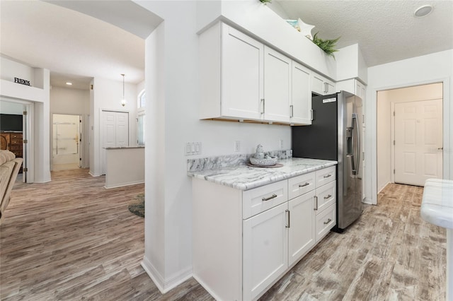 kitchen with stainless steel refrigerator with ice dispenser, white cabinetry, a textured ceiling, and light hardwood / wood-style flooring