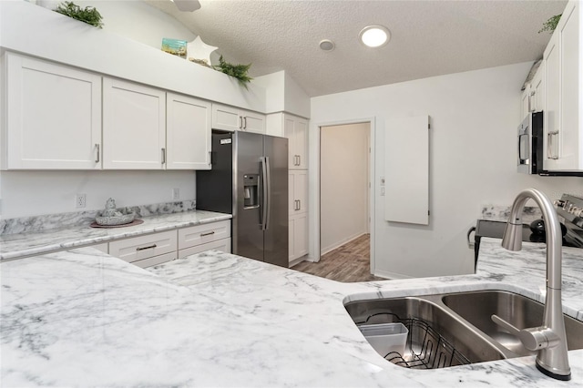 kitchen featuring white cabinetry, sink, light stone counters, stainless steel appliances, and a textured ceiling