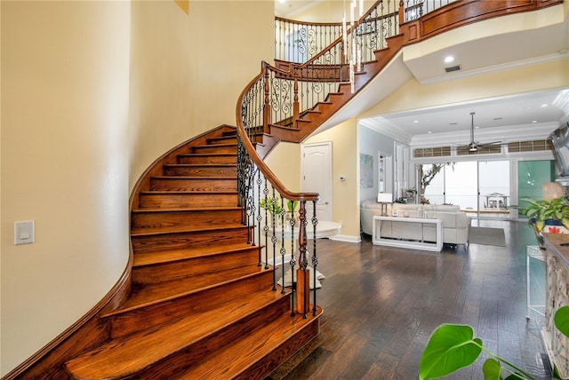 stairs featuring baseboards, visible vents, a towering ceiling, ornamental molding, and wood finished floors