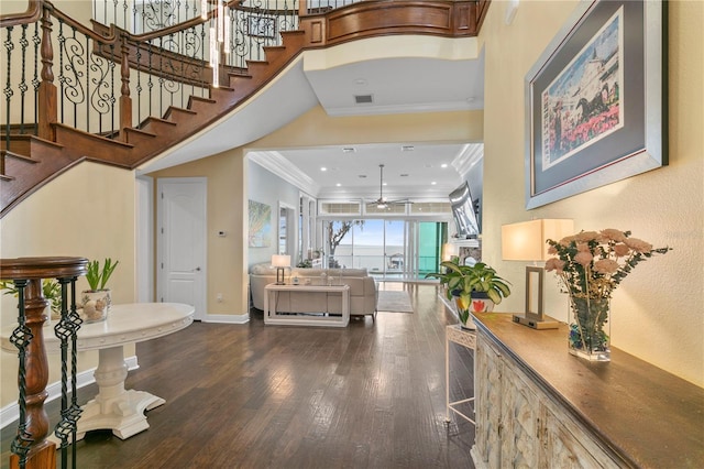 entryway with wood finished floors, a ceiling fan, a towering ceiling, baseboards, and ornamental molding