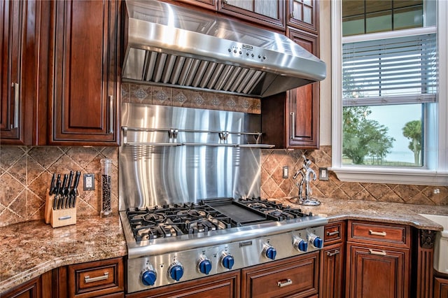 kitchen featuring stainless steel gas stovetop, light stone counters, backsplash, and under cabinet range hood