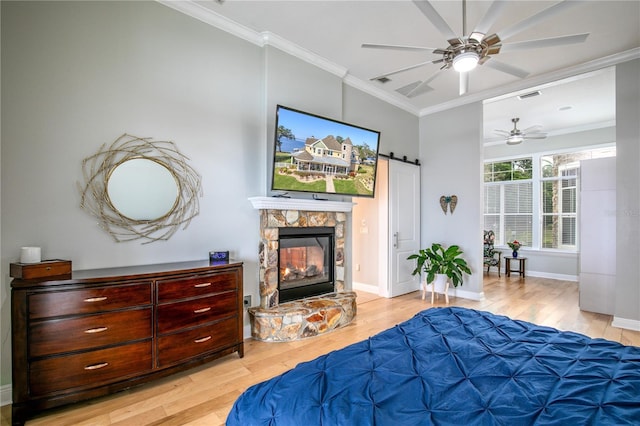 bedroom with a barn door, visible vents, wood finished floors, crown molding, and a stone fireplace