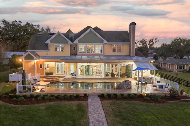 back of property at dusk featuring a yard, a chimney, a patio, an outdoor fire pit, and a fenced backyard