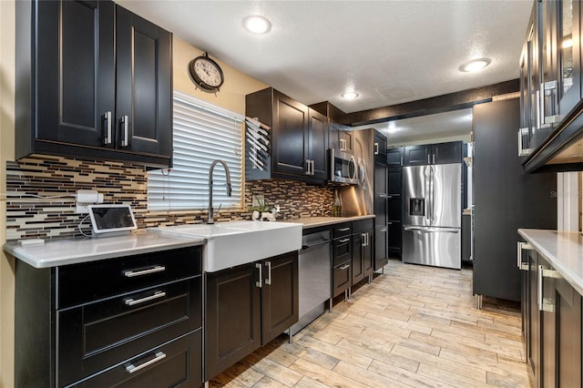 kitchen featuring sink, a textured ceiling, light wood-type flooring, stainless steel appliances, and decorative backsplash