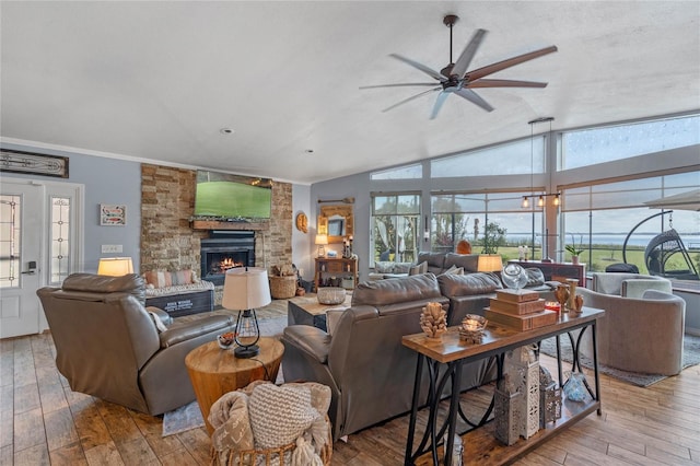 living room featuring ceiling fan, a stone fireplace, vaulted ceiling, and light wood-type flooring