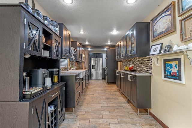 kitchen featuring dark brown cabinetry, stainless steel fridge, decorative backsplash, and a textured ceiling