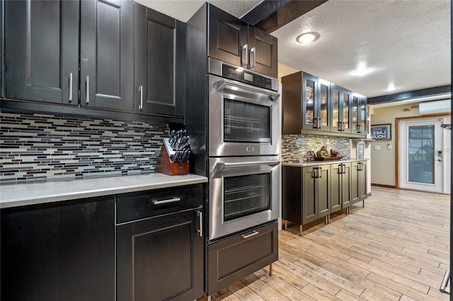 kitchen featuring an AC wall unit, tasteful backsplash, light wood-type flooring, stainless steel double oven, and a textured ceiling