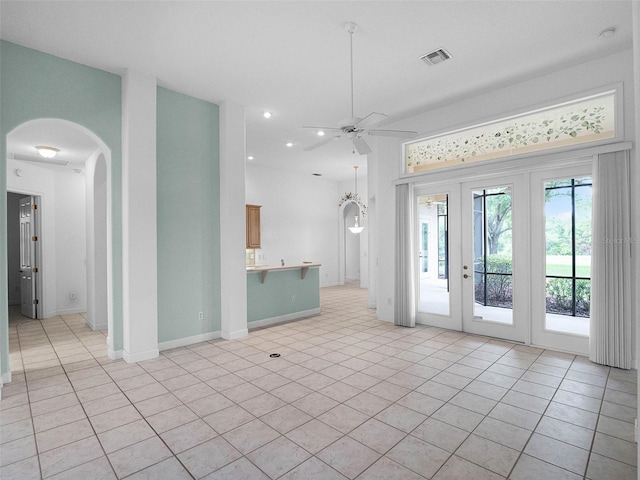 unfurnished living room with light tile patterned floors, arched walkways, a ceiling fan, visible vents, and baseboards