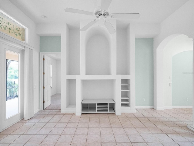 interior space featuring built in shelves, baseboards, arched walkways, ceiling fan, and light tile patterned flooring