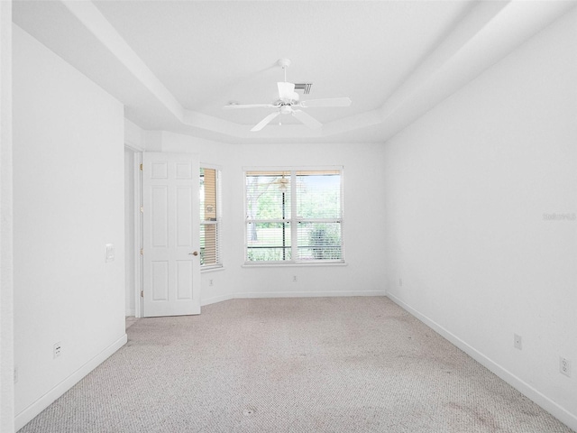 spare room with baseboards, a raised ceiling, light carpet, and a ceiling fan