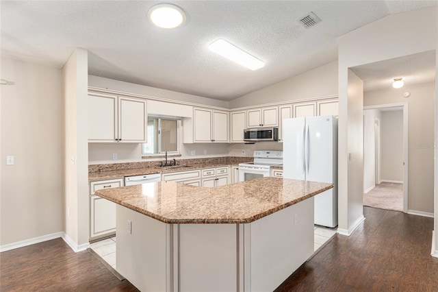 kitchen with a kitchen island, white appliances, vaulted ceiling, and light stone countertops