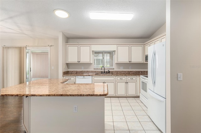 kitchen with white appliances, sink, light tile patterned flooring, a kitchen island, and light stone countertops