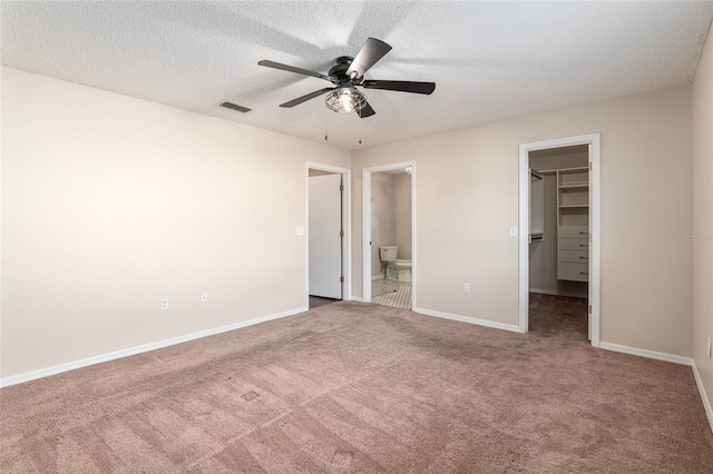 unfurnished bedroom featuring a closet, a walk in closet, carpet flooring, a textured ceiling, and connected bathroom