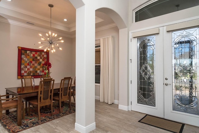 entryway featuring a notable chandelier, a raised ceiling, crown molding, light wood-type flooring, and french doors