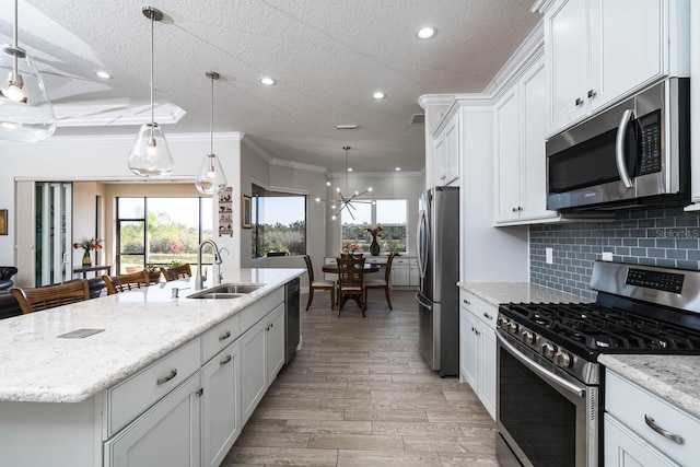 kitchen featuring sink, white cabinetry, decorative light fixtures, appliances with stainless steel finishes, and a kitchen island with sink