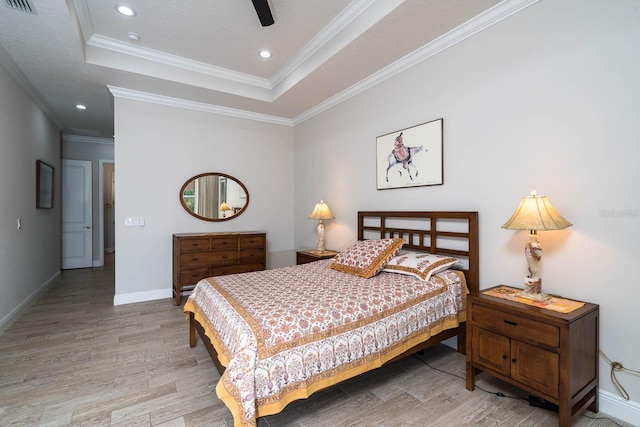 bedroom with crown molding, light hardwood / wood-style flooring, ceiling fan, and a tray ceiling