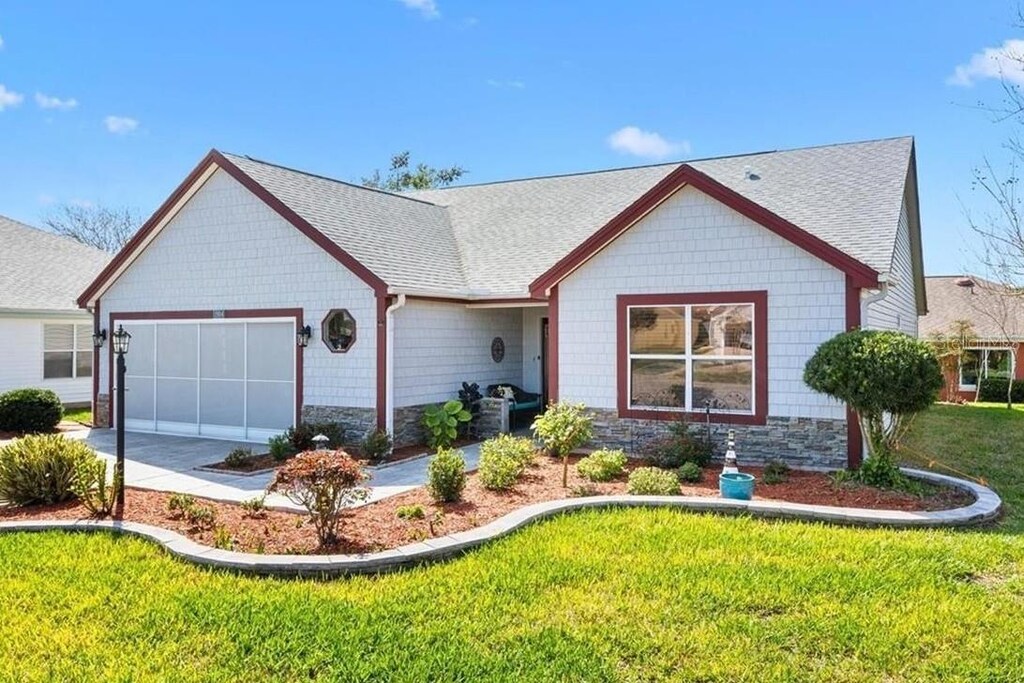 view of front of home featuring stone siding, a front yard, a garage, and roof with shingles