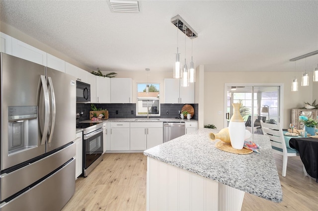 kitchen with pendant lighting, appliances with stainless steel finishes, a center island, and white cabinets