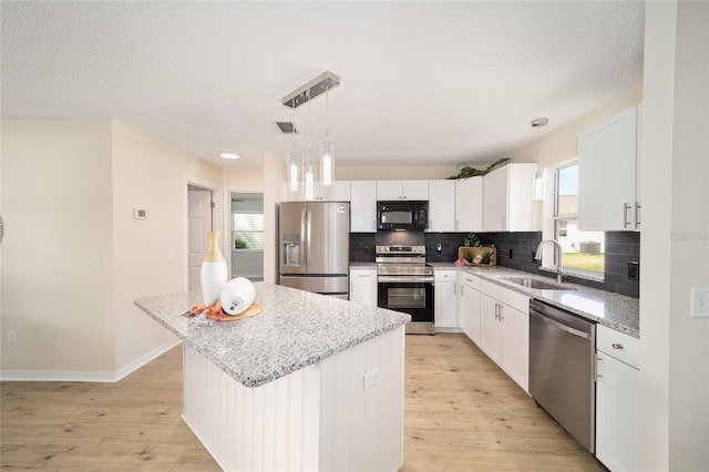 kitchen with appliances with stainless steel finishes, white cabinetry, sink, hanging light fixtures, and a center island