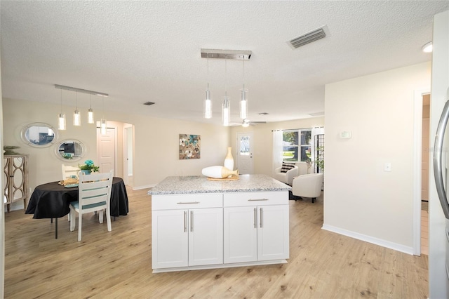 kitchen with white cabinetry, light stone countertops, pendant lighting, and light hardwood / wood-style flooring