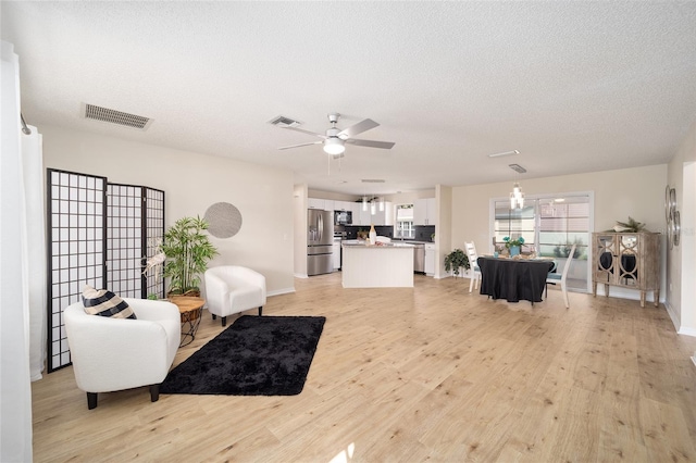 living room with ceiling fan, a textured ceiling, and light wood-type flooring