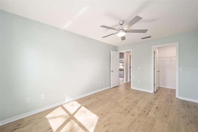 unfurnished bedroom with a spacious closet, light hardwood / wood-style flooring, a textured ceiling, a closet, and ceiling fan