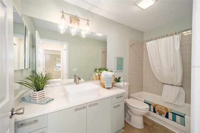 full bathroom with hardwood / wood-style floors, vanity, toilet, shower / bathtub combination with curtain, and a textured ceiling