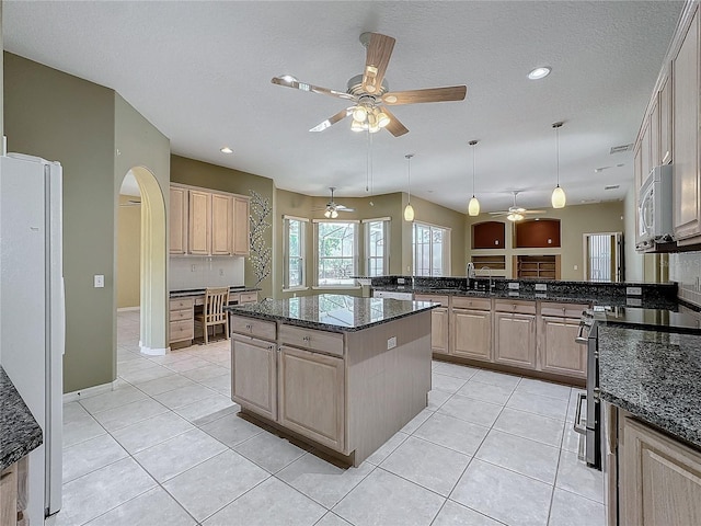 kitchen featuring a center island, hanging light fixtures, dark stone countertops, light brown cabinets, and white appliances