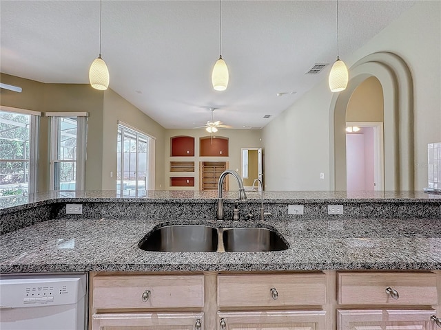 kitchen featuring sink, decorative light fixtures, light brown cabinets, dark stone countertops, and white dishwasher