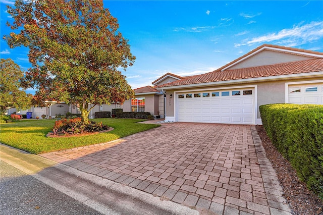 ranch-style home featuring decorative driveway, stucco siding, an attached garage, a tiled roof, and a front lawn