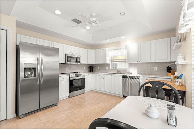 kitchen featuring a sink, white cabinetry, light countertops, appliances with stainless steel finishes, and a raised ceiling