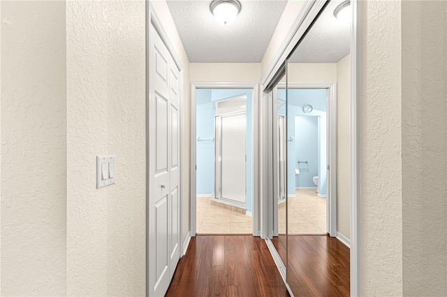 corridor with a textured wall, a textured ceiling, and wood finished floors