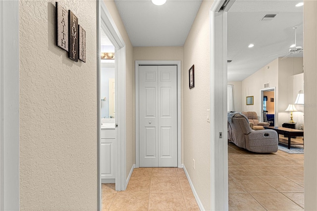 hall featuring a textured wall, light tile patterned flooring, and visible vents