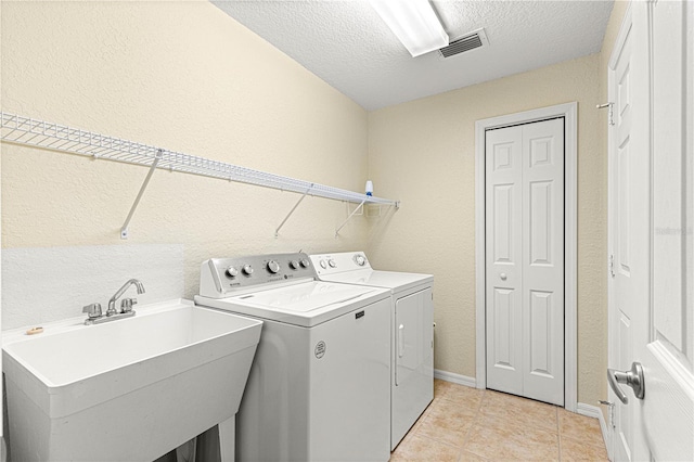 washroom featuring laundry area, visible vents, a textured ceiling, washing machine and dryer, and a sink