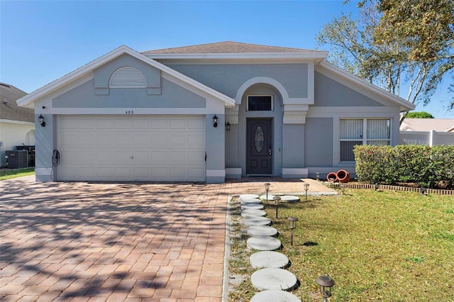 ranch-style home with a garage, central AC unit, decorative driveway, a front lawn, and stucco siding