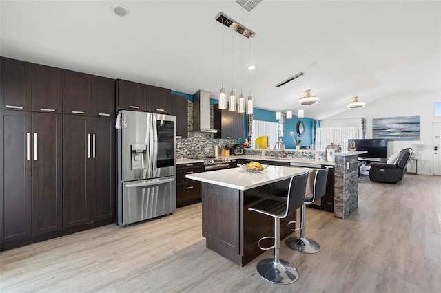 kitchen featuring a peninsula, vaulted ceiling, stainless steel appliances, light countertops, and wall chimney range hood