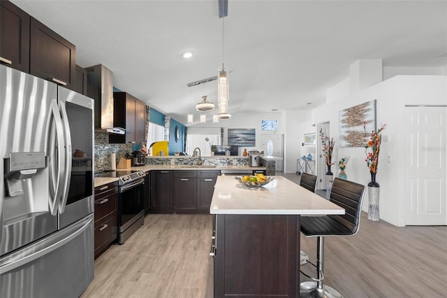 kitchen with a breakfast bar area, stainless steel appliances, light wood-style floors, light countertops, and wall chimney exhaust hood