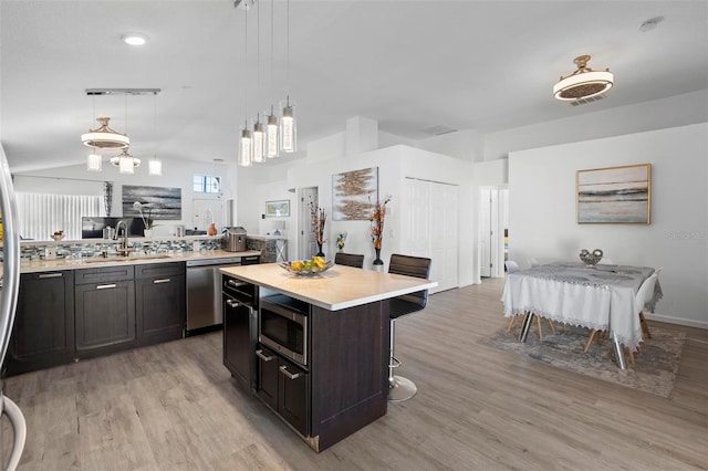 kitchen with a sink, light countertops, appliances with stainless steel finishes, light wood finished floors, and a kitchen bar