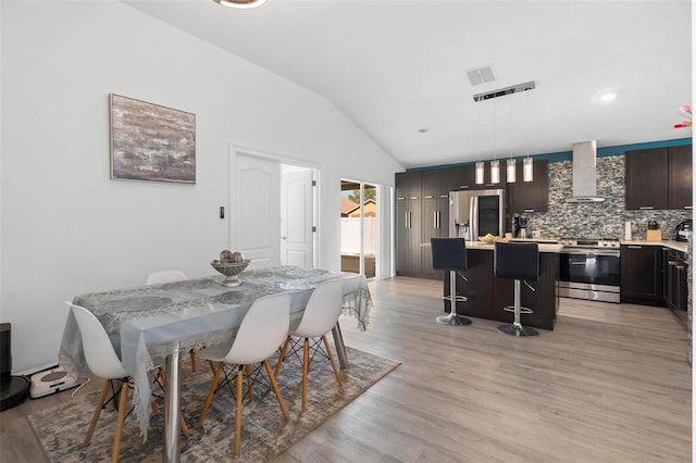 dining room with light wood finished floors, visible vents, and vaulted ceiling