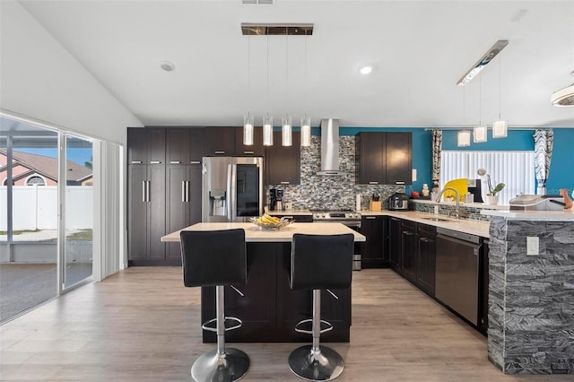 kitchen with wall chimney exhaust hood, a breakfast bar area, stainless steel appliances, light countertops, and a sink