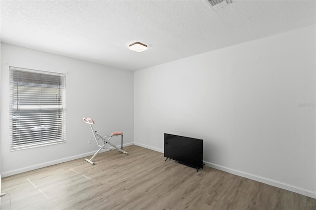 unfurnished room with visible vents, a textured ceiling, baseboards, and wood finished floors