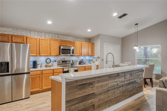 kitchen featuring appliances with stainless steel finishes, sink, hanging light fixtures, and light hardwood / wood-style flooring