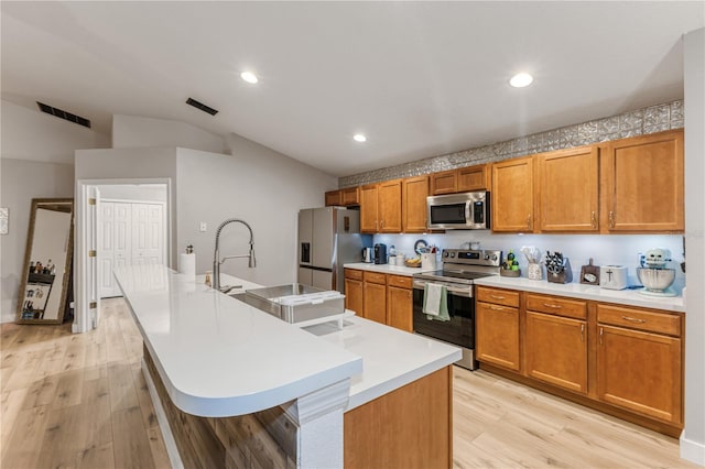 kitchen featuring lofted ceiling, a kitchen bar, light wood-type flooring, appliances with stainless steel finishes, and a kitchen island with sink